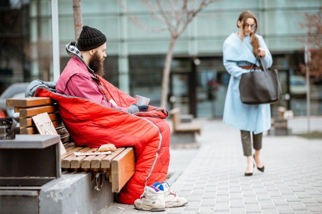 Homeless begging money while sitting on the bench with passing by businesswoman near the business center