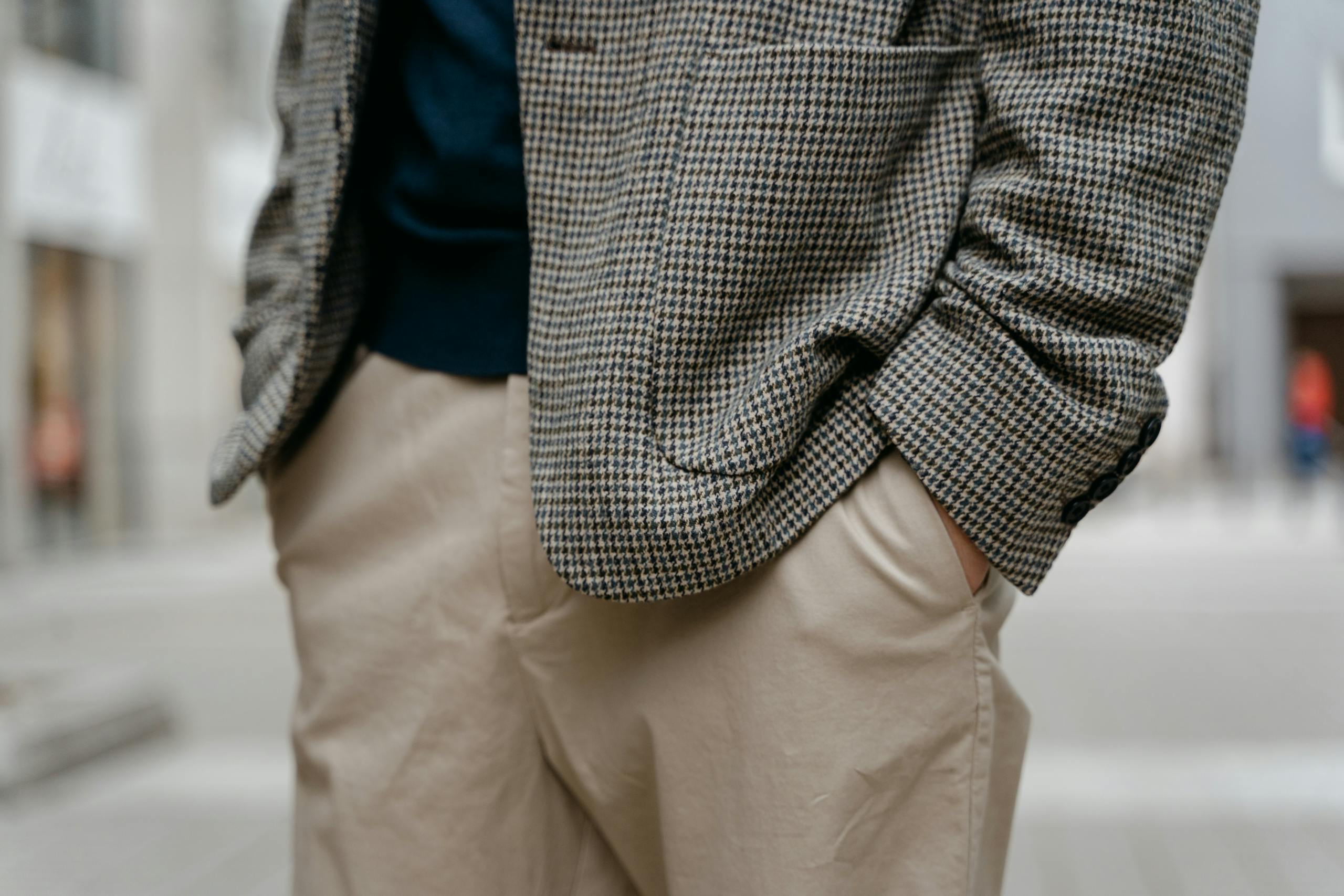 Close-up of a man's stylish outfit with a checkered blazer and tan pants, outdoors.