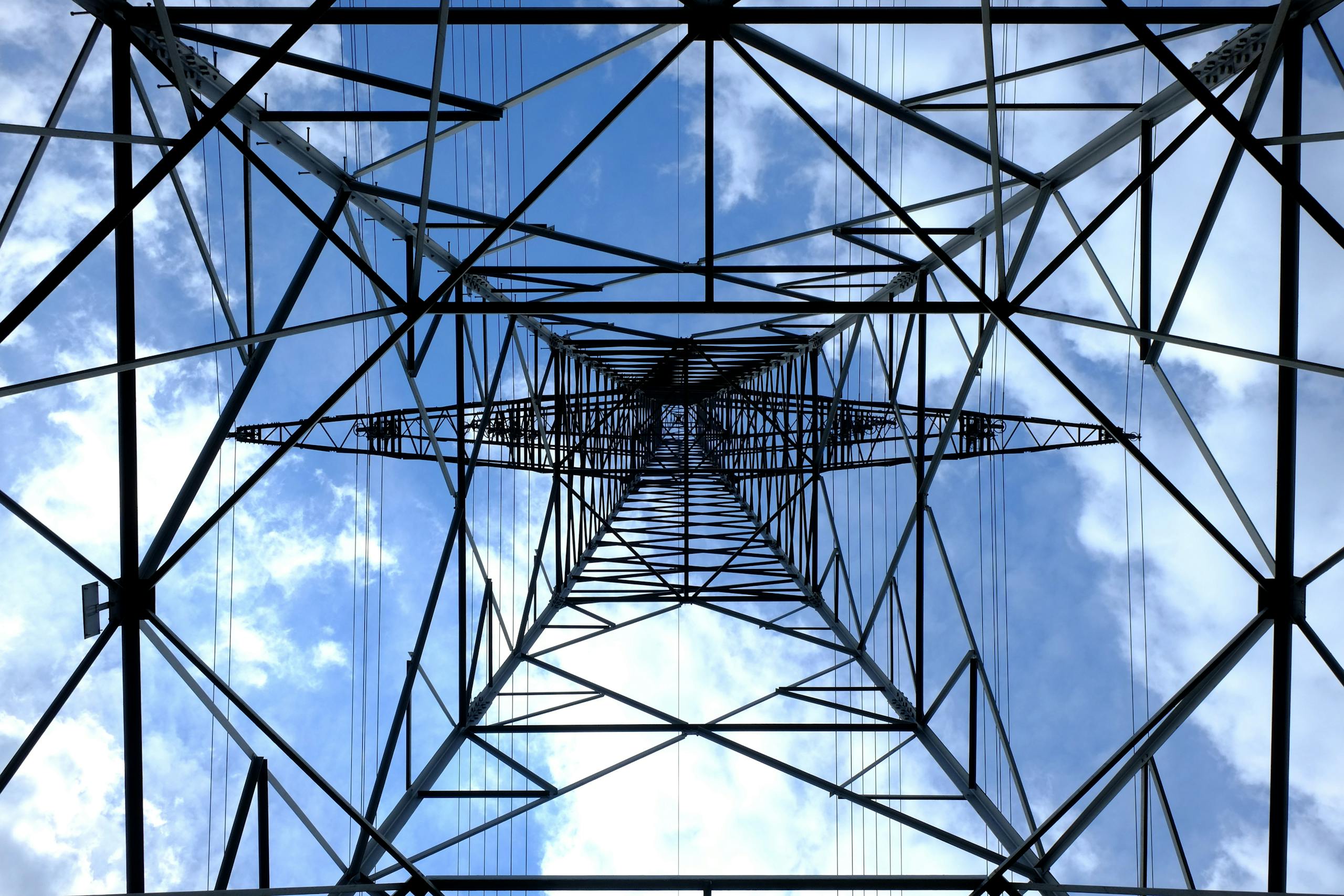 Looking up at a steel power pylon against a bright blue sky.